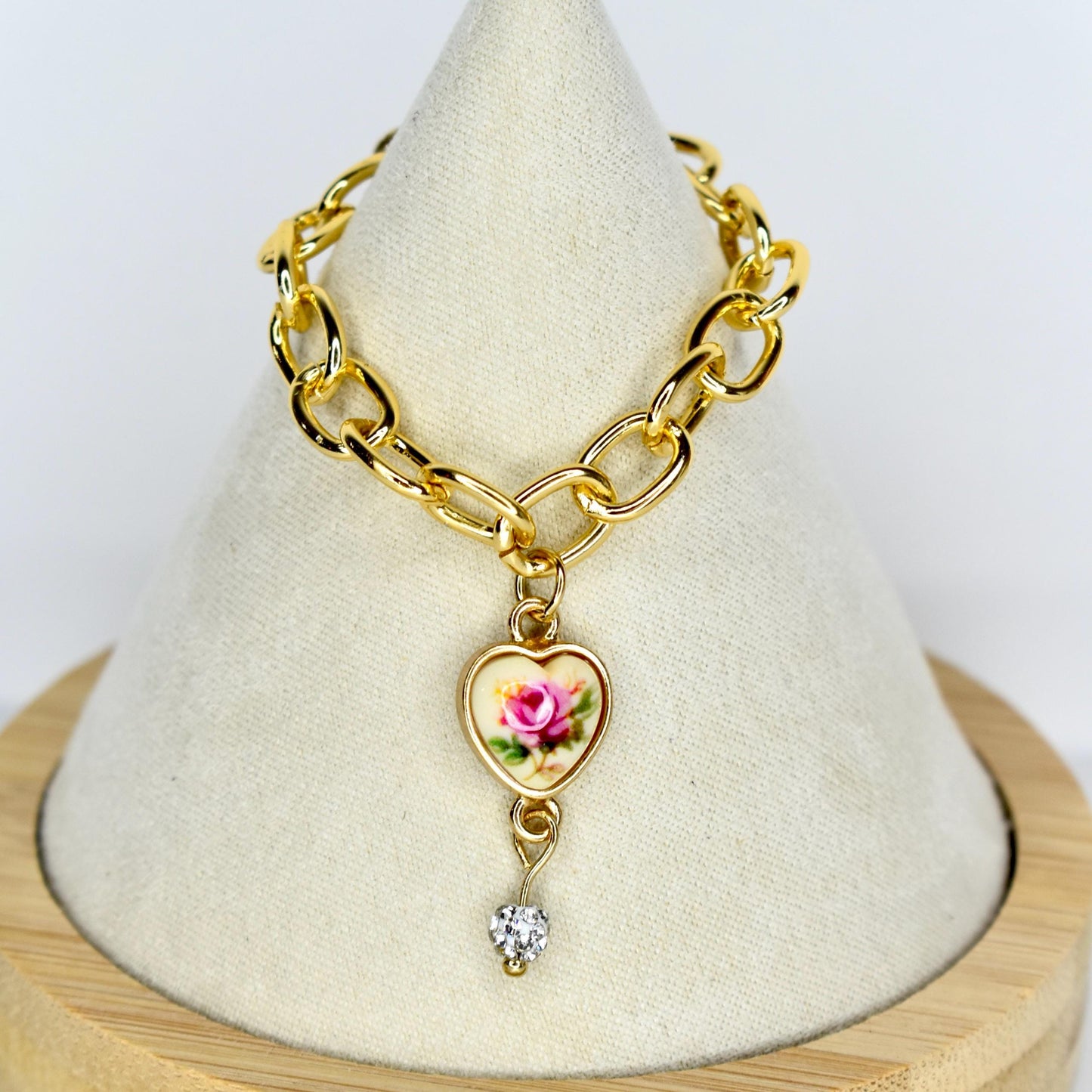 Gold-toned chain 17cm monster doll necklace with a heart-shaped pendant. The pendant features a pink rose design on a cream background, framed by a gold border. A small, clear, heart-shaped gem hangs below the pendant. The necklace is displayed on a white surface.