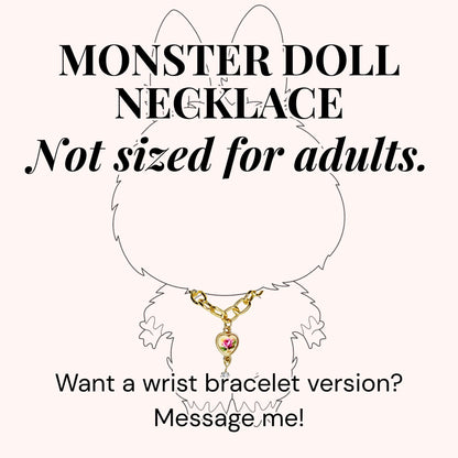 A gold-colored necklace with a heart-shaped pendant featuring a pink rose design. The image includes the text "MONSTER DOLL NECKLACE" and "Not sized for adults." The text "Want a wrist bracelet version? Message me!" is also present.