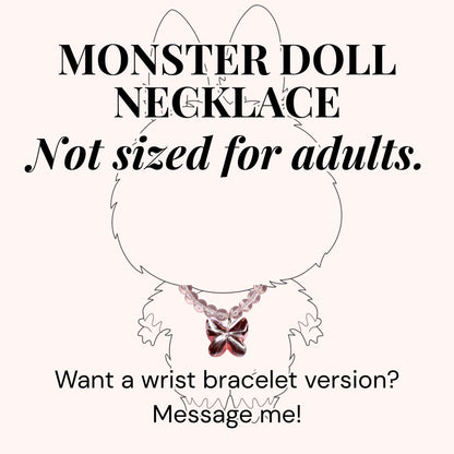 A pink necklace with a butterfly pendant is displayed on a cartoon monster illustration. The text reads "MONSTER DOLL NECKLACE" and "Not sized for adults." Additional text asks about a wrist bracelet version and to message the seller.