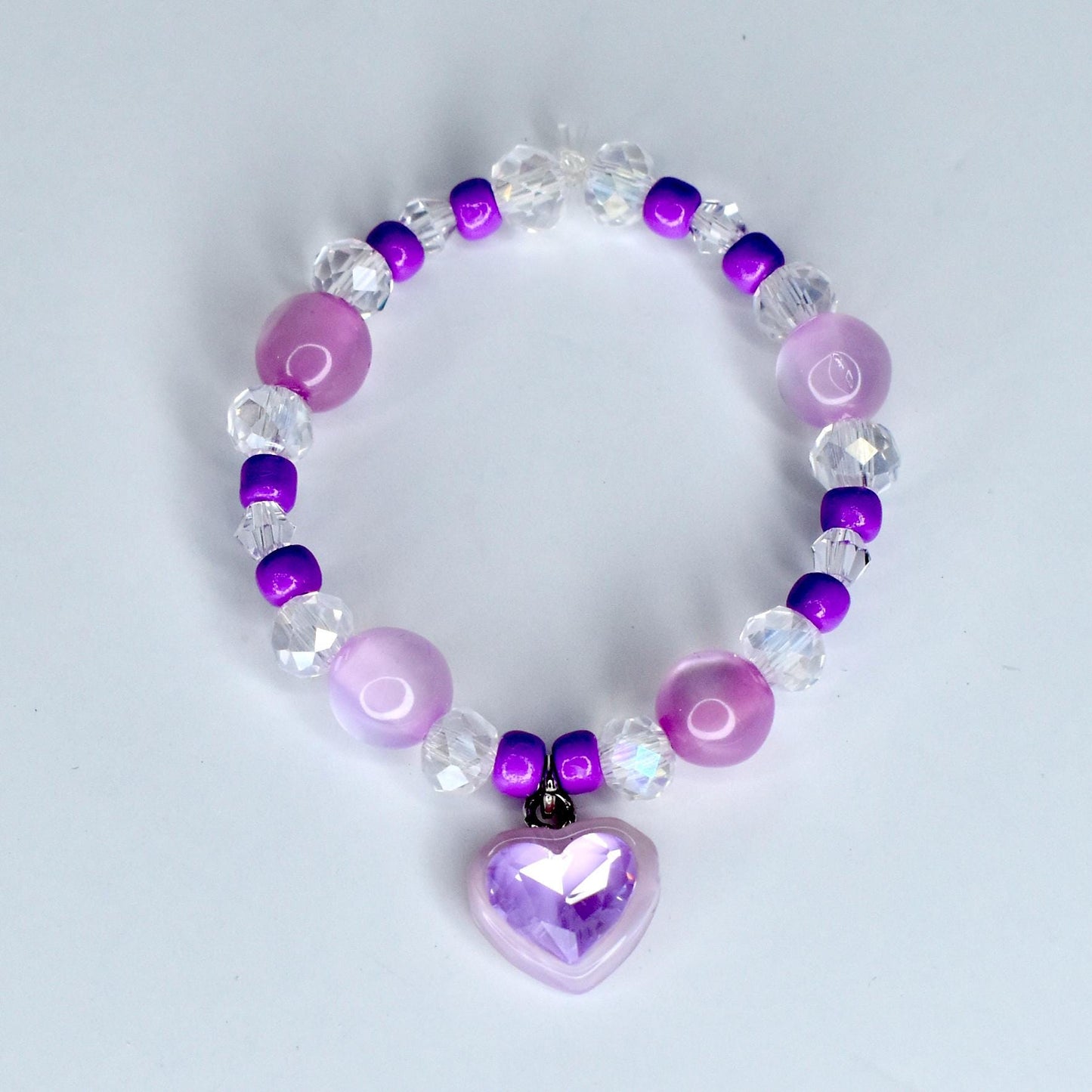 A beaded 17cm monster doll necklace featuring a heart charm. The necklace is composed of various beads in shades of purple, clear, and white. The heart charm is a light purple color and has a faceted design.