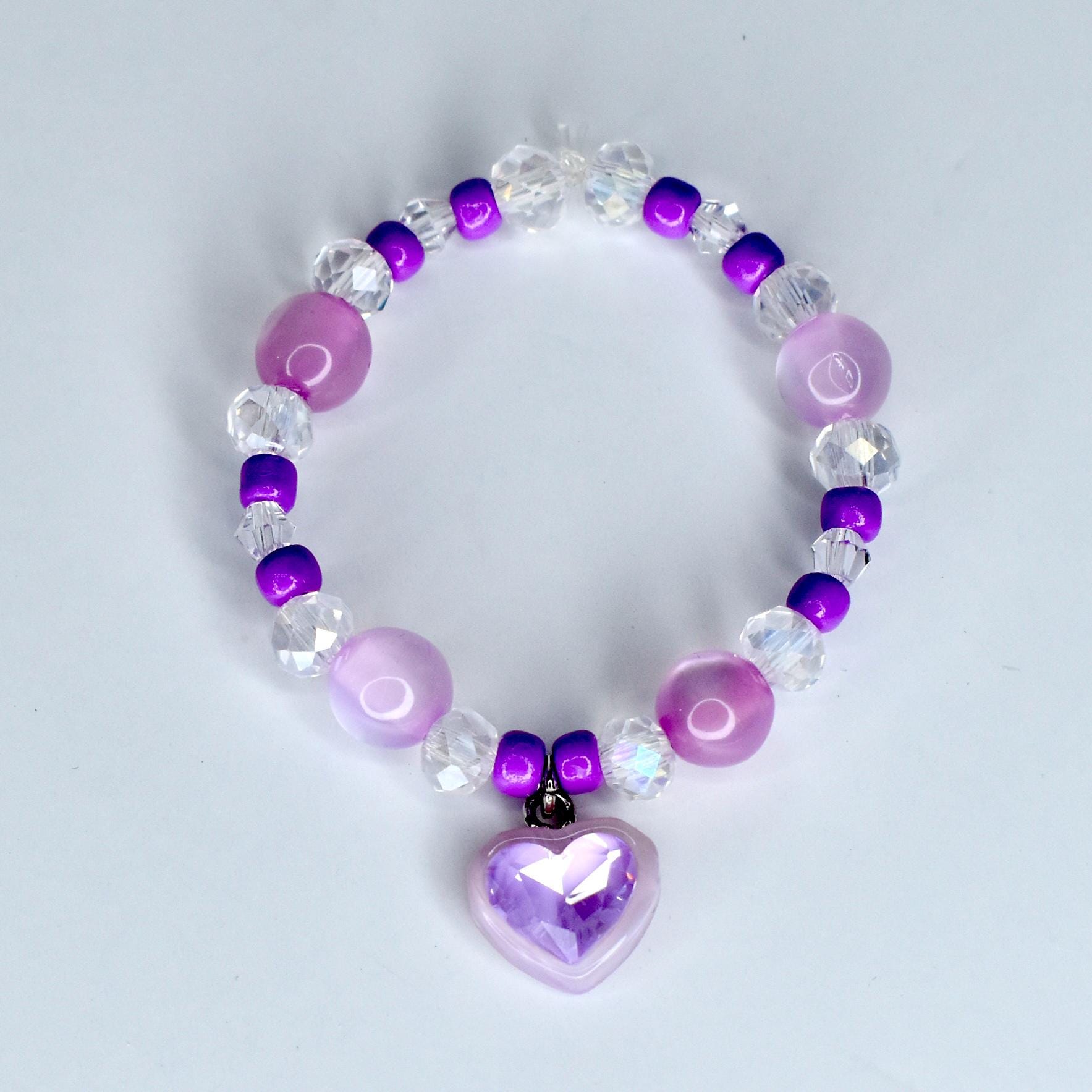 A beaded 17cm monster doll necklace featuring a heart charm. The necklace is composed of various beads in shades of purple, clear, and white. The heart charm is a light purple color and has a faceted design.
