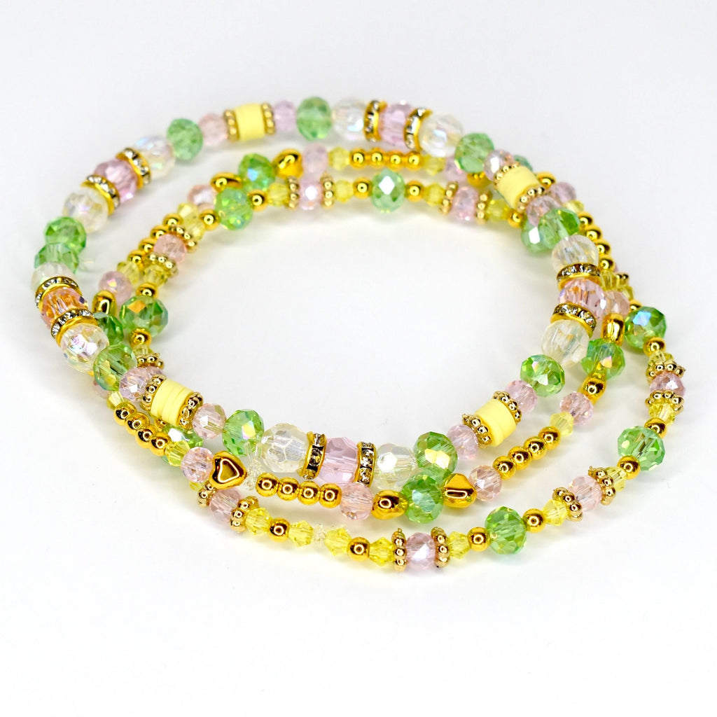 Three beaded bracelets in shades of pink, green, yellow, and clear. The bracelets feature gold-colored accents and small heart-shaped charms. The beads are various shapes and sizes, creating a layered effect.