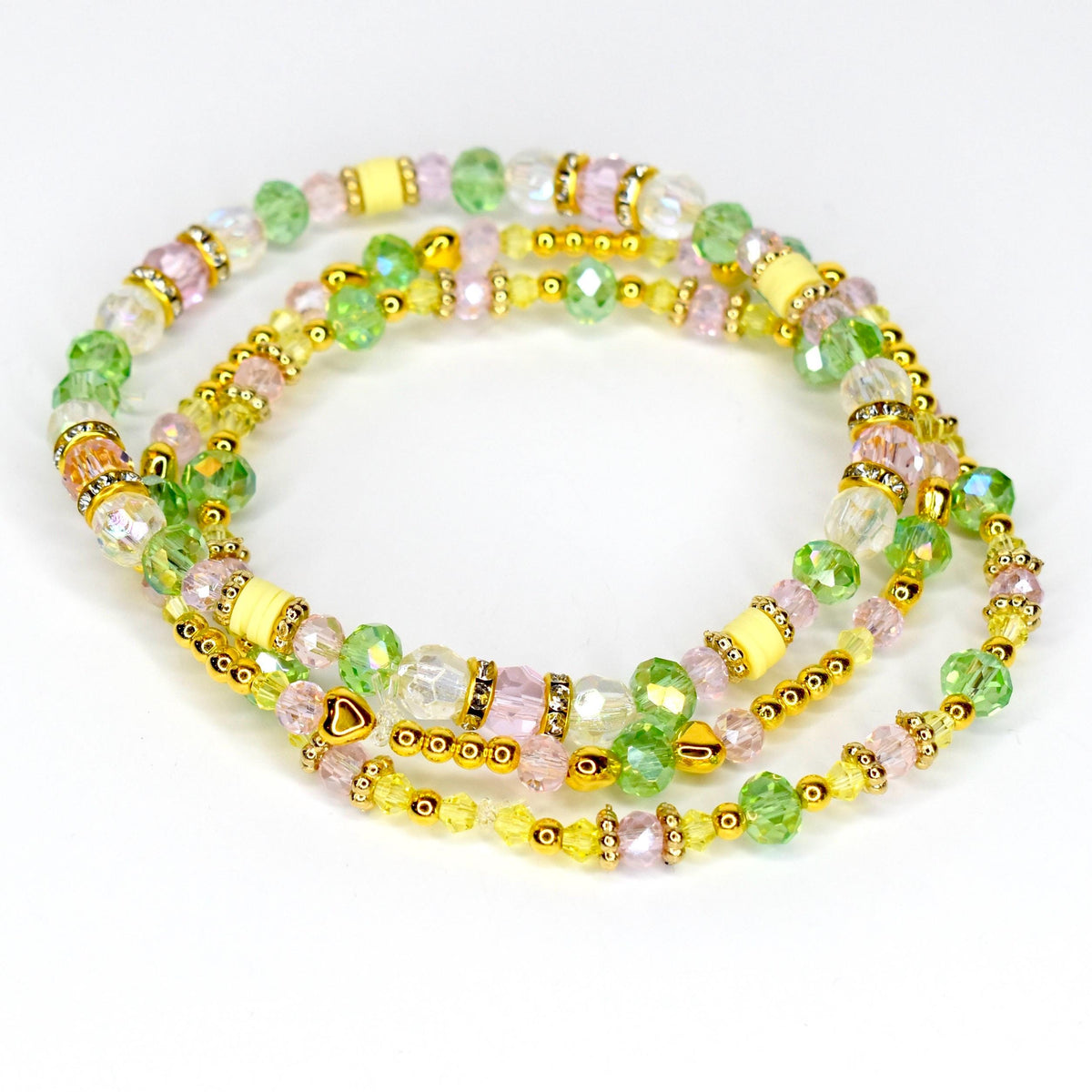Three beaded bracelets in shades of pink, green, yellow, and clear. The bracelets feature gold-colored accents and small heart-shaped charms. The beads are various shapes and sizes, creating a layered effect.