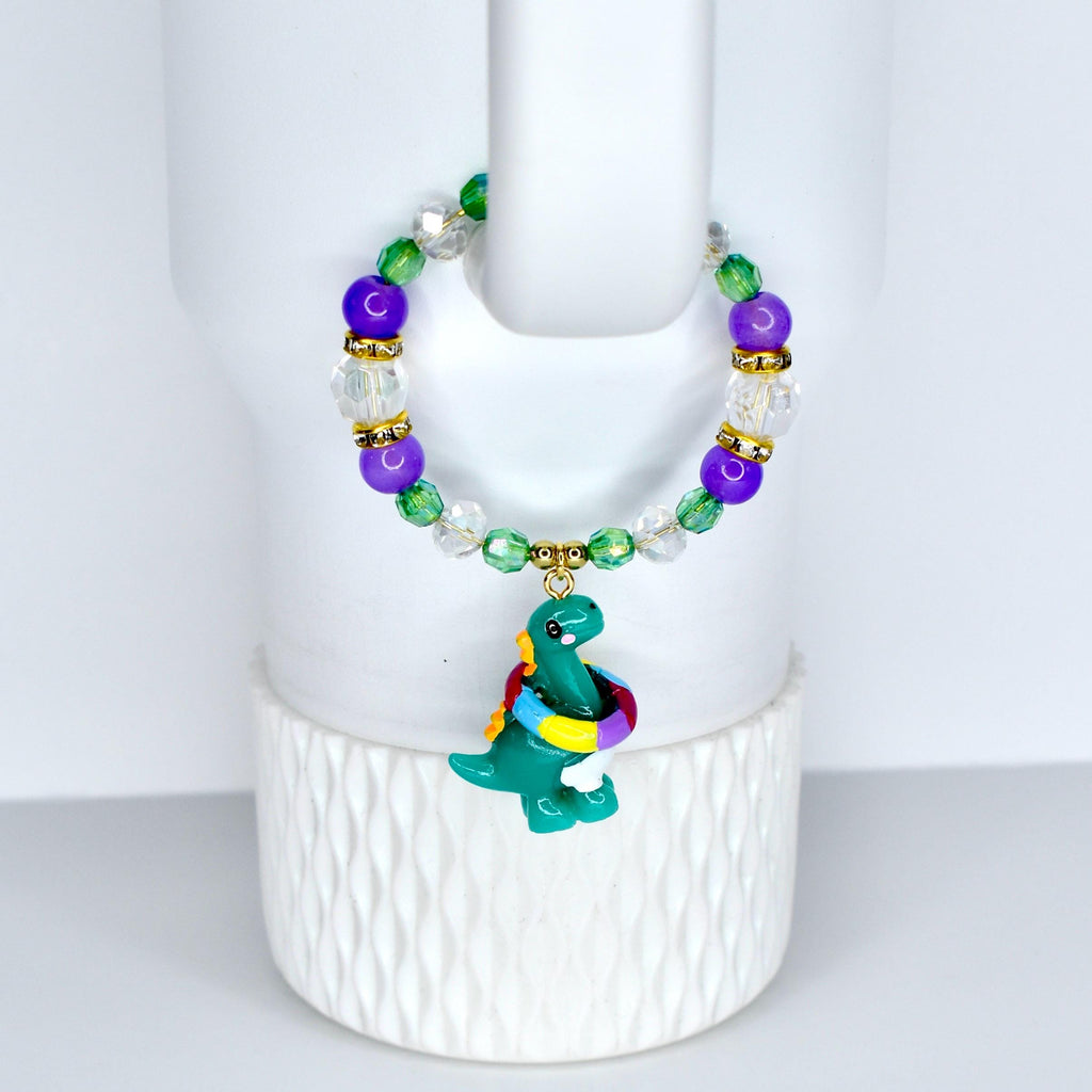 A beaded bracelet with a green dinosaur charm. The bracelet features purple, green, and clear beads with gold accents.