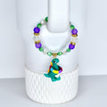 A beaded bracelet with a green dinosaur charm. The bracelet features purple, green, and clear beads with gold accents.