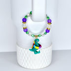 A beaded bracelet with a green dinosaur charm. The bracelet features purple, green, and clear beads with gold accents.