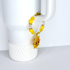 A yellow beaded tumbler handle bracelet with a gold sun charm. The bracelet features yellow and clear beads, with a gold clasp. The sun charm has a smiling face and is surrounded by gold rays.
