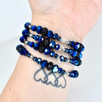 A collection of wrap bracelets featuring faceted blue beads, interspersed with silver-toned beads and black, textured beads. The bracelets are wrapped around a wrist, showcasing the varying textures and colors.