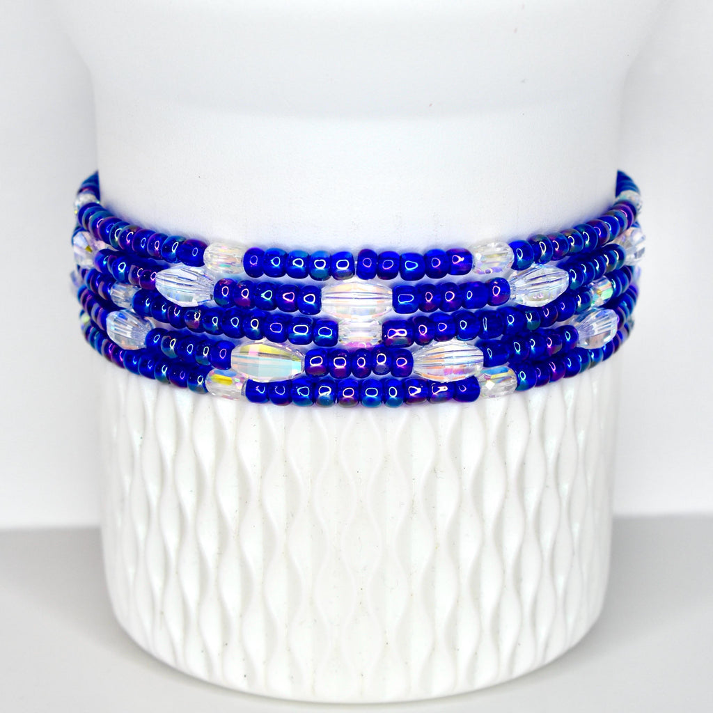A beaded bracelet with multiple strands of small, dark blue beads and iridescent, oval-shaped beads. The bracelet is wrapped around a white, textured ceramic vase. The beads are arranged in a repeating pattern.