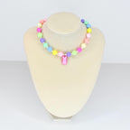 A colorful beaded necklace with pastel-colored beads in shades of pink, yellow, green, blue, and purple. A pink bunny charm hangs from the center. The necklace is displayed on a white mannequin.