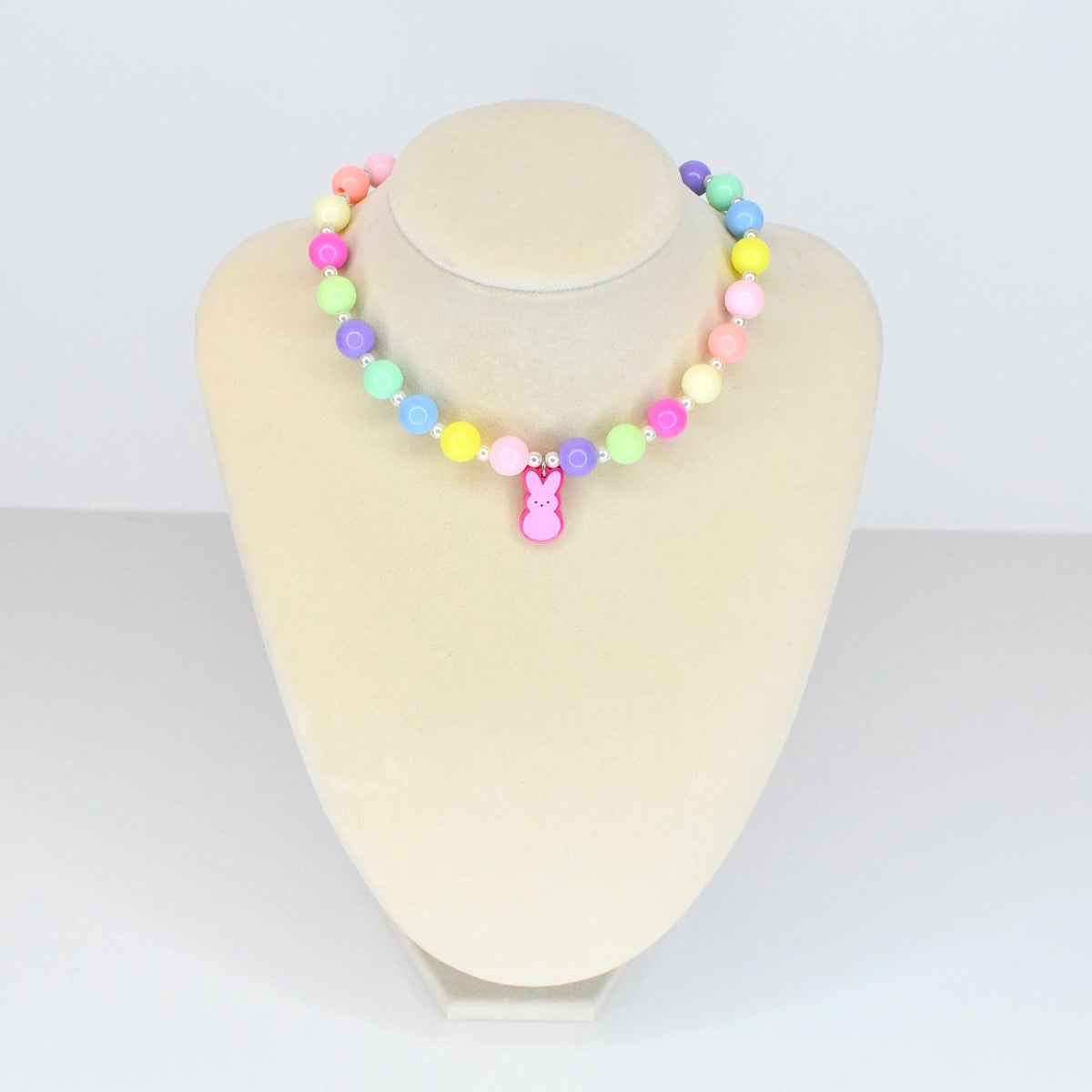 A colorful beaded necklace with pastel-colored beads in shades of pink, yellow, green, blue, and purple. A pink bunny charm hangs from the center. The necklace is displayed on a white mannequin.