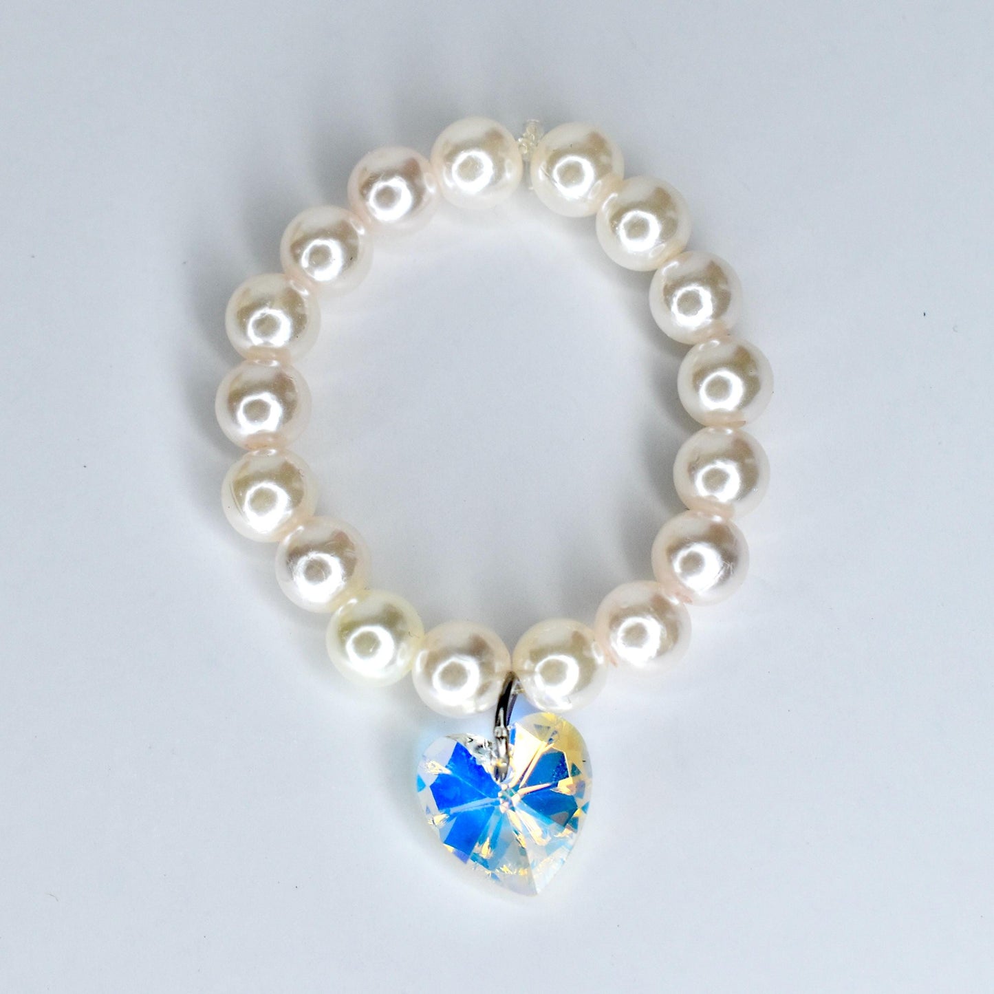 A pearl 17cm monster doll necklace with a heart-shaped pendant. The necklace features round, off-white pearls strung together. The pendant is a clear crystal with a blue and yellow iridescent effect, shaped like a heart.