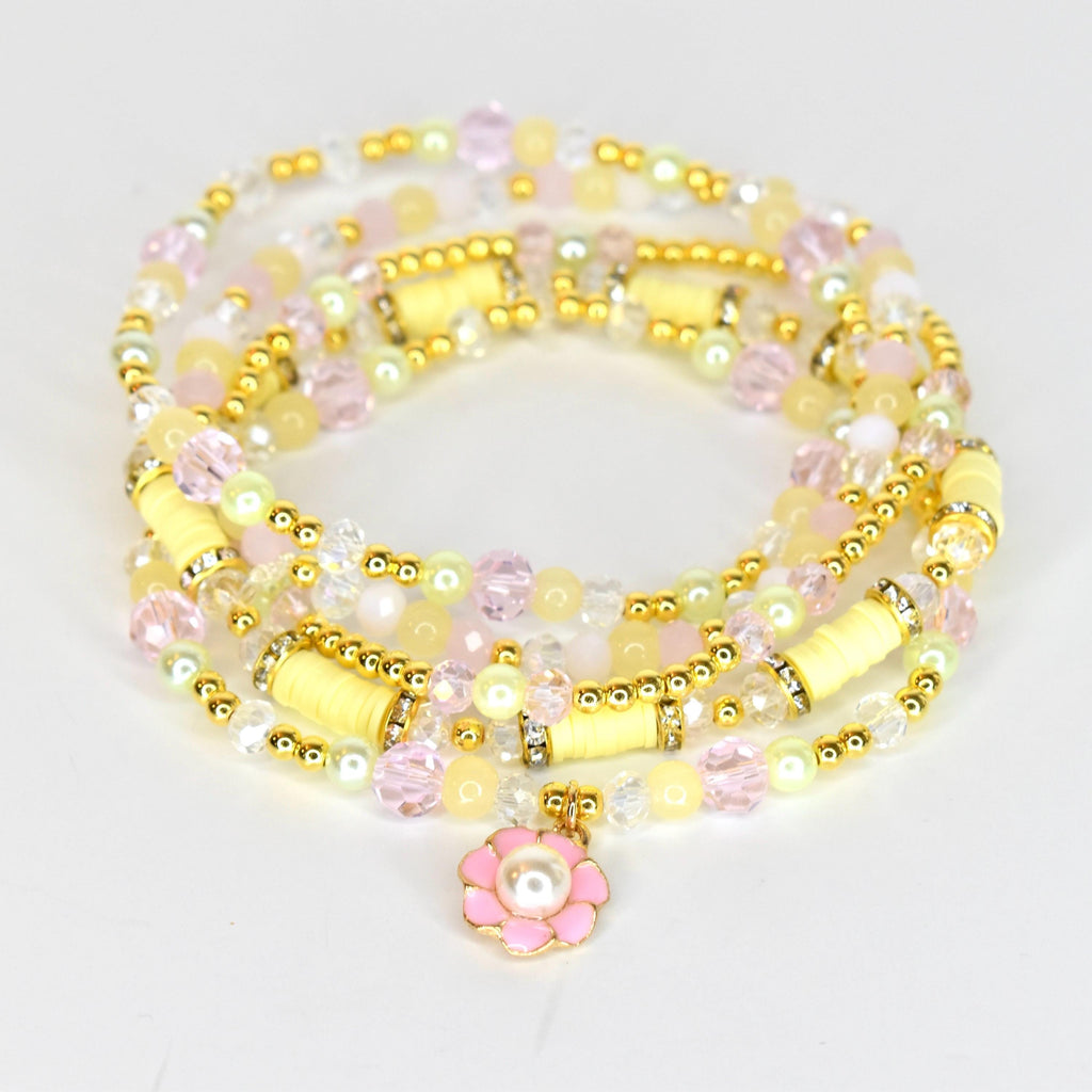 A multi-strand bracelet featuring a variety of beads in pastel yellow, pink, and clear colors. Gold-toned accents and cylindrical yellow beads are interspersed throughout. A pink flower charm with a pearl center dangles from the bracelet.