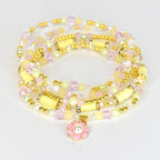 A multi-strand bracelet featuring a variety of beads in pastel yellow, pink, and clear colors. Gold-toned accents and cylindrical yellow beads are interspersed throughout. A pink flower charm with a pearl center dangles from the bracelet.