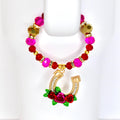A tumbler handle beaded bracelet with a gold horseshoe charm. The tumbler bracelet features pink, red, and gold beads. The horseshoe charm is adorned with clear crystals and red roses with green leaves.