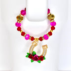 A tumbler handle beaded bracelet with a gold horseshoe charm. The tumbler bracelet features pink, red, and gold beads. The horseshoe charm is adorned with clear crystals and red roses with green leaves.