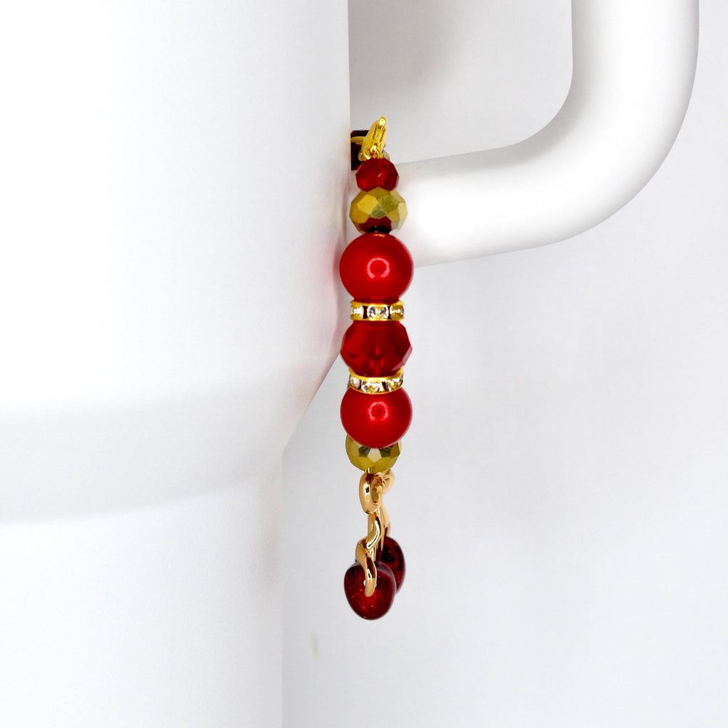 A tumbler handle charm with a gold-colored hook and chain. The charm features a series of red and gold beads, including round and faceted shapes. The bottom of the charm has a cherry charm.