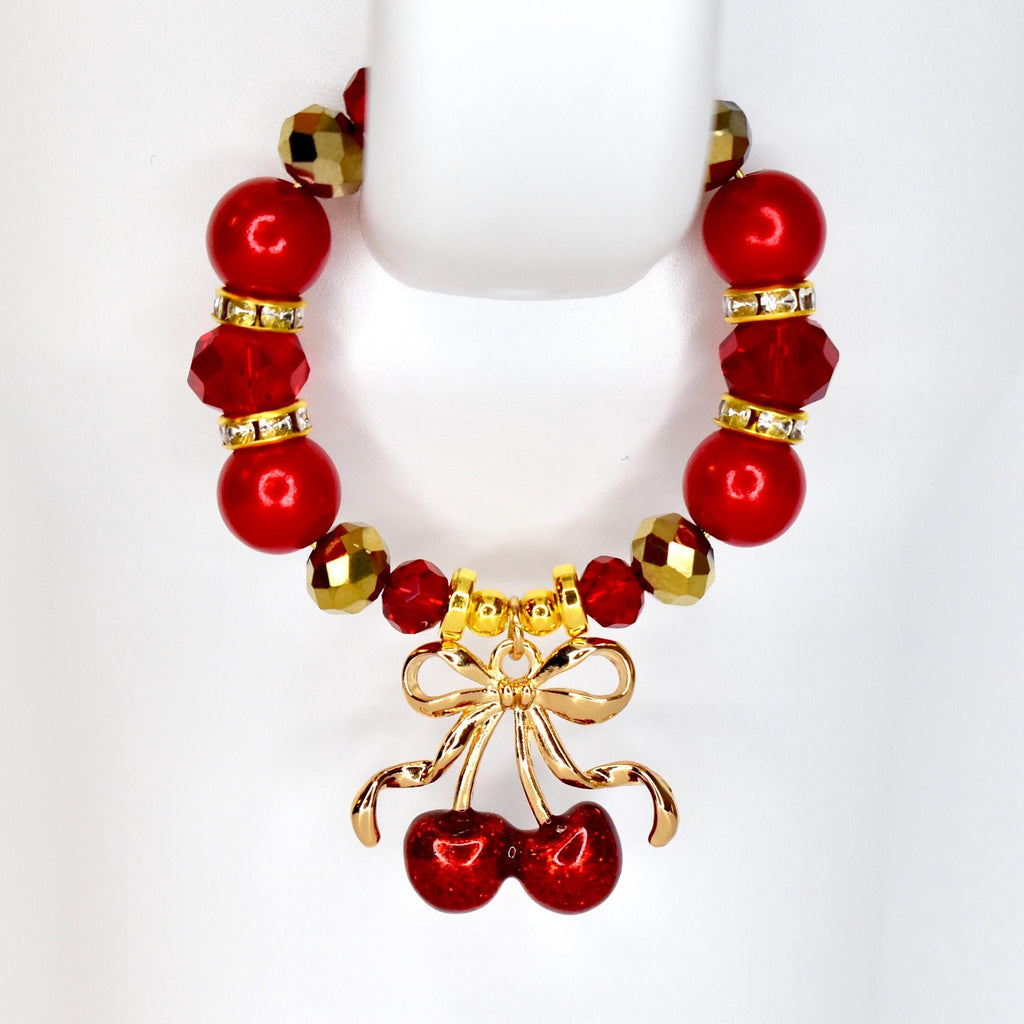 A red beaded tumbler handle bracelet with gold accents and a cherry charm. The bracelet features large red beads, smaller gold beads, and a gold cherry charm with a bow. The bracelet is designed to go around the handle of a tumbler.