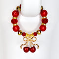 A red beaded tumbler handle bracelet with gold accents and a cherry charm. The bracelet features large red beads, smaller gold beads, and a gold cherry charm with a bow. The bracelet is designed to go around the handle of a tumbler.