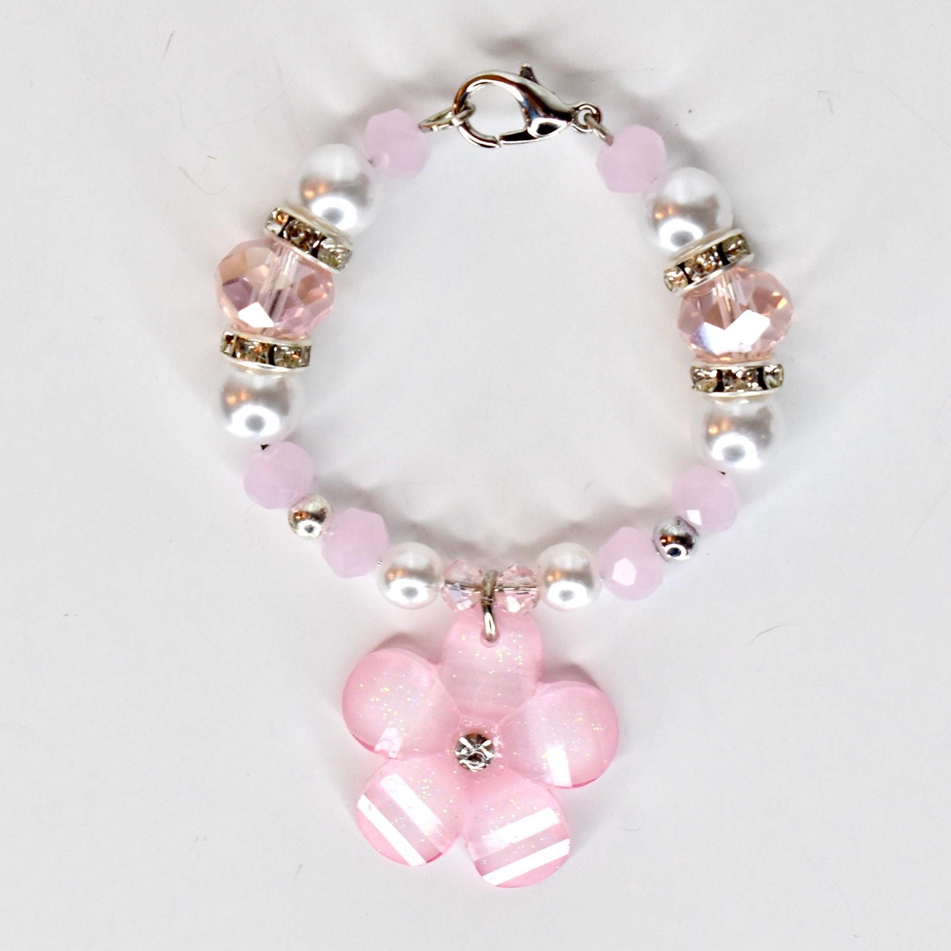 A pink and white beaded tumbler handle bracelet with a flower charm. The tumbler charm features pink and white beads, clear crystal accents, and a silver clasp. The flower charm is pink with white stripes and a crystal center.