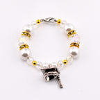 A beaded tumbler handle charm featuring large white faux pearls, clear iridescent beads, and gold-colored accents. The bracelet includes a silver-colored graduation cap charm with a tassel, perfect for a graduation gift.