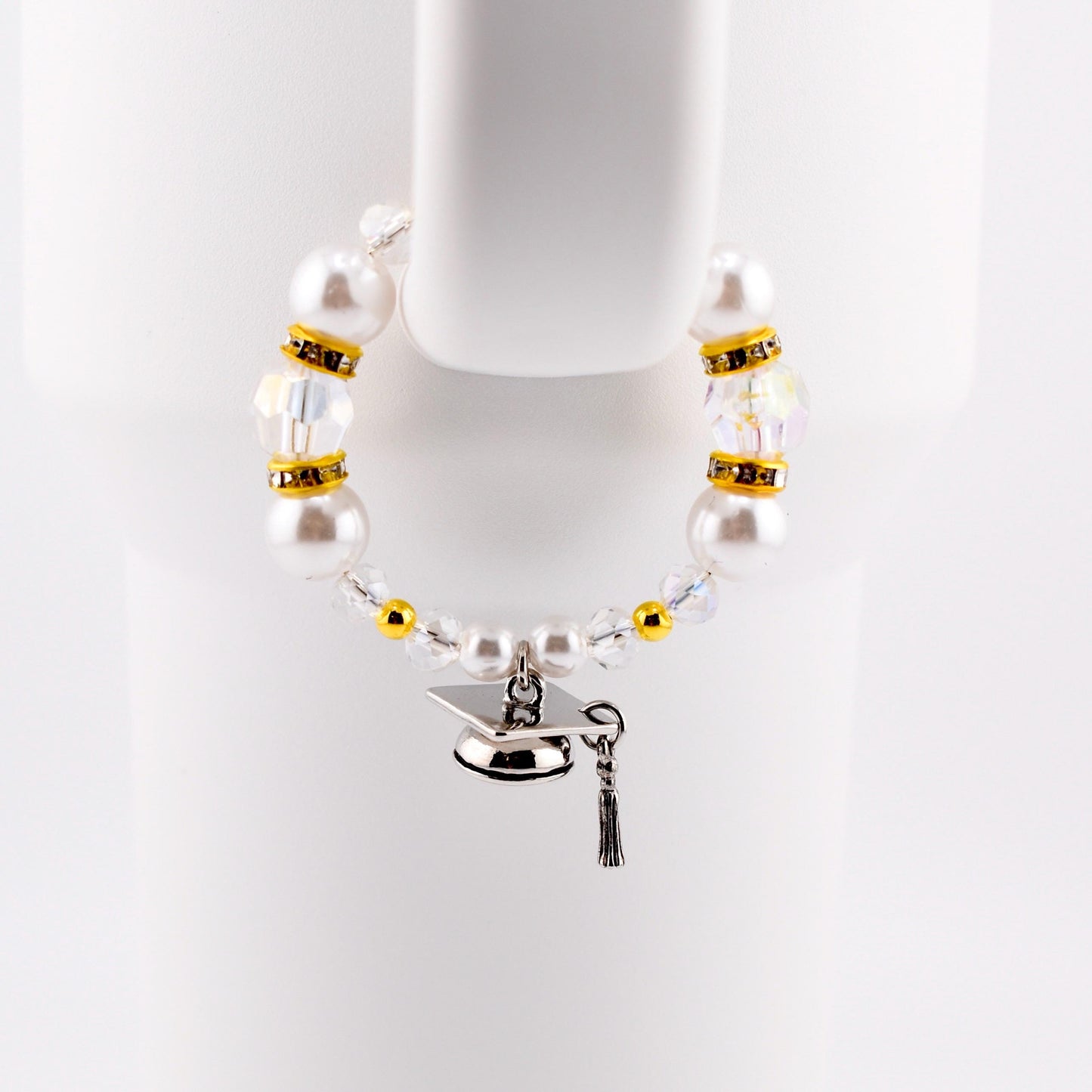 A graduation-themed tumbler handle bracelet featuring large white faux pearls, clear crystal beads, and gold accents. A silver graduation cap charm with a black tassel hangs from the bracelet. The bracelet is displayed against a white background.