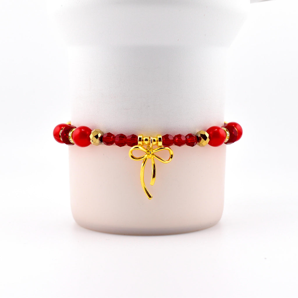 Red beaded bracelet with gold accents and a gold bow charm. The bracelet features a mix of round and faceted beads. The bow charm hangs from the center of the bracelet, adding a touch of elegance.