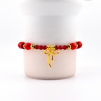 Red beaded bracelet with gold accents and a gold bow charm. The bracelet features a mix of round and faceted beads. The bow charm hangs from the center of the bracelet, adding a touch of elegance.