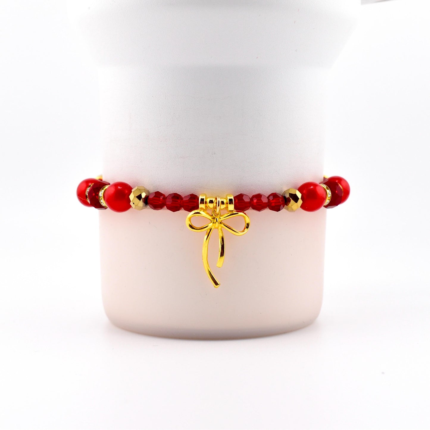 Red beaded bracelet with gold accents and a gold bow charm. The bracelet features a mix of round and faceted beads. The bow charm hangs from the center of the bracelet, adding a touch of elegance.
