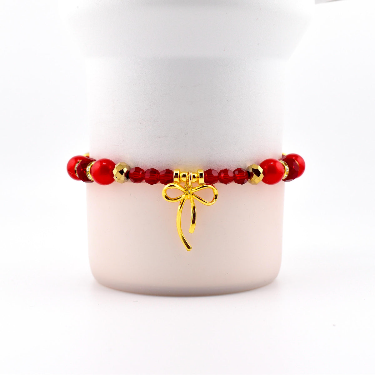 Red beaded bracelet with gold accents and a gold bow charm. The bracelet features a mix of round and faceted beads. The bow charm hangs from the center of the bracelet, adding a touch of elegance.