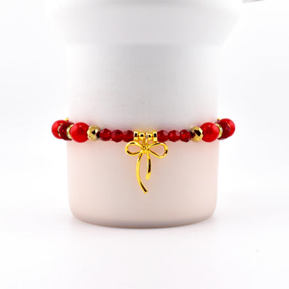Red beaded bracelet with gold accents and a gold bow charm. The bracelet features a mix of round and faceted beads. The bow charm hangs from the center of the bracelet, adding a touch of elegance.