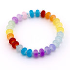 A rainbow-colored beaded bracelet. The bracelet features a variety of colorful beads, including red, orange, yellow, green, blue, and purple. The beads are strung together on a silver-colored elastic cord.