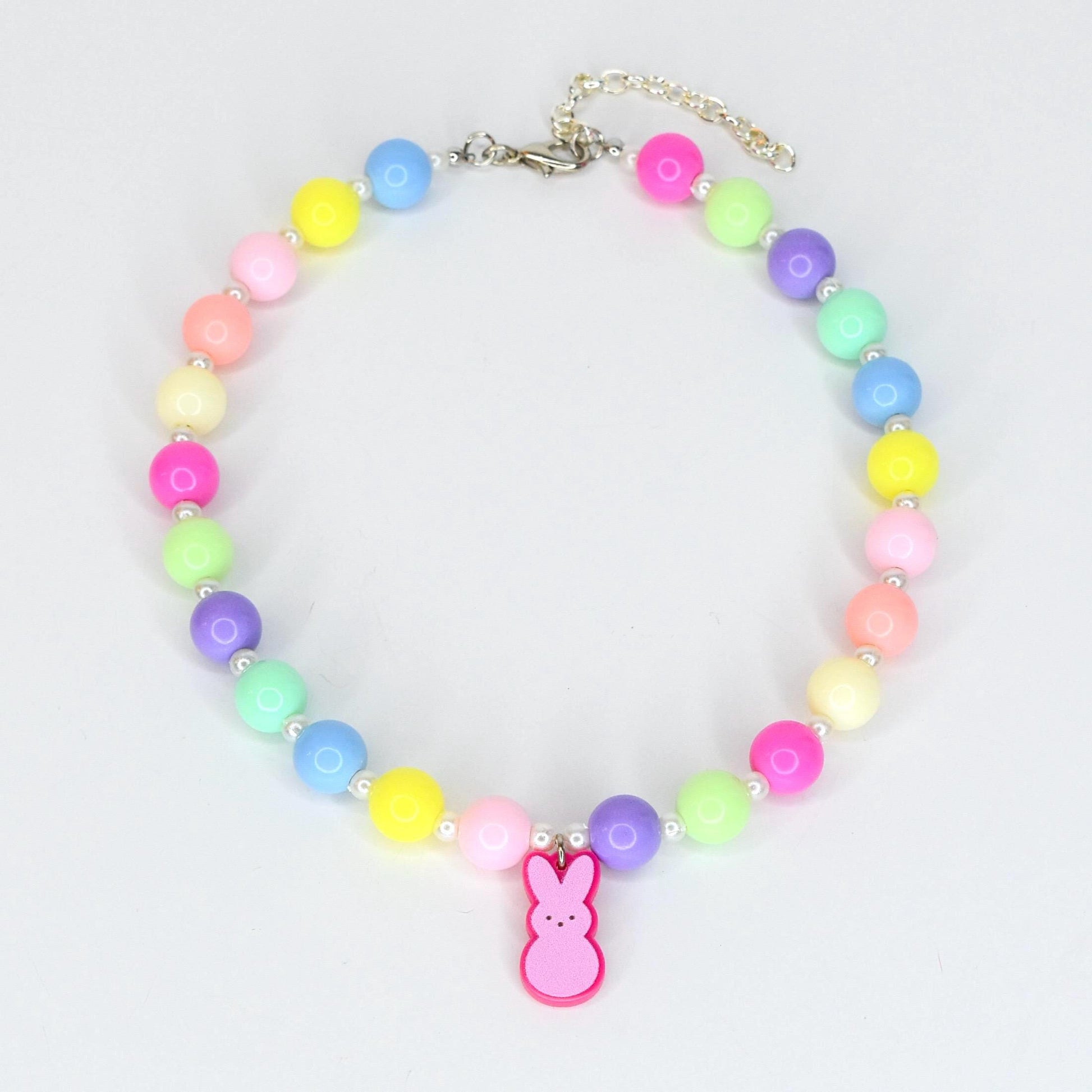 A colorful beaded necklace featuring a variety of pastel-colored beads, including pink, yellow, blue, green, and purple. A pink bunny charm hangs from the center. The necklace is secured with a silver-colored clasp.
