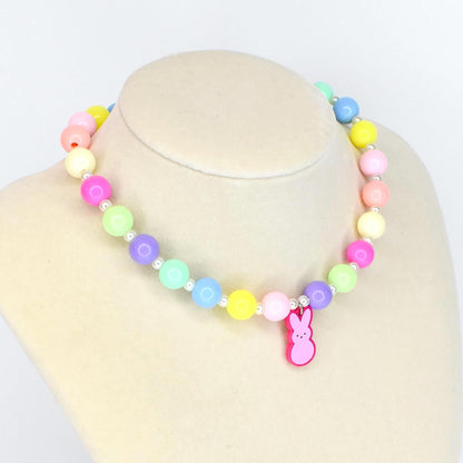 A colorful beaded necklace with pastel-colored beads in shades of pink, yellow, green, blue, and purple. A pink bunny charm hangs from the necklace. The necklace is displayed on a white mannequin.