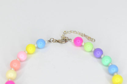 A colorful necklace featuring large, round beads in pastel shades of pink, yellow, blue, green, and purple. The necklace has a silver-toned chain and clasp, and small white beads are interspersed between the larger beads.