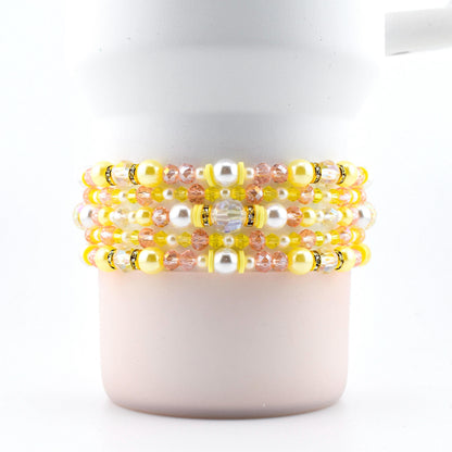 A set of five handmade beaded bracelets in yellow, pink and pearl.