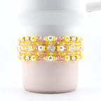 A set of five handmade beaded bracelets in yellow, pink and pearl.