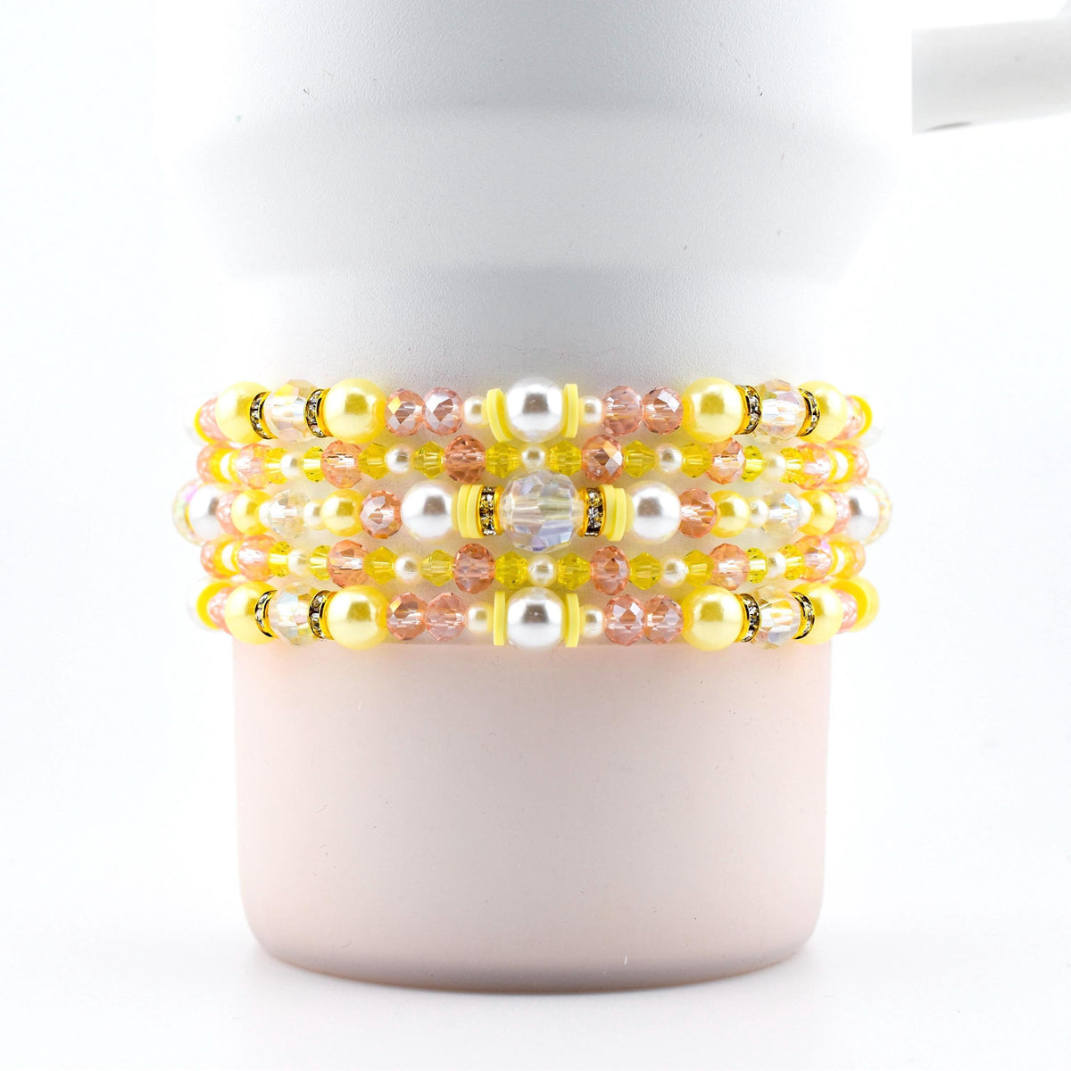 A set of five handmade beaded bracelets in yellow, pink and pearl.