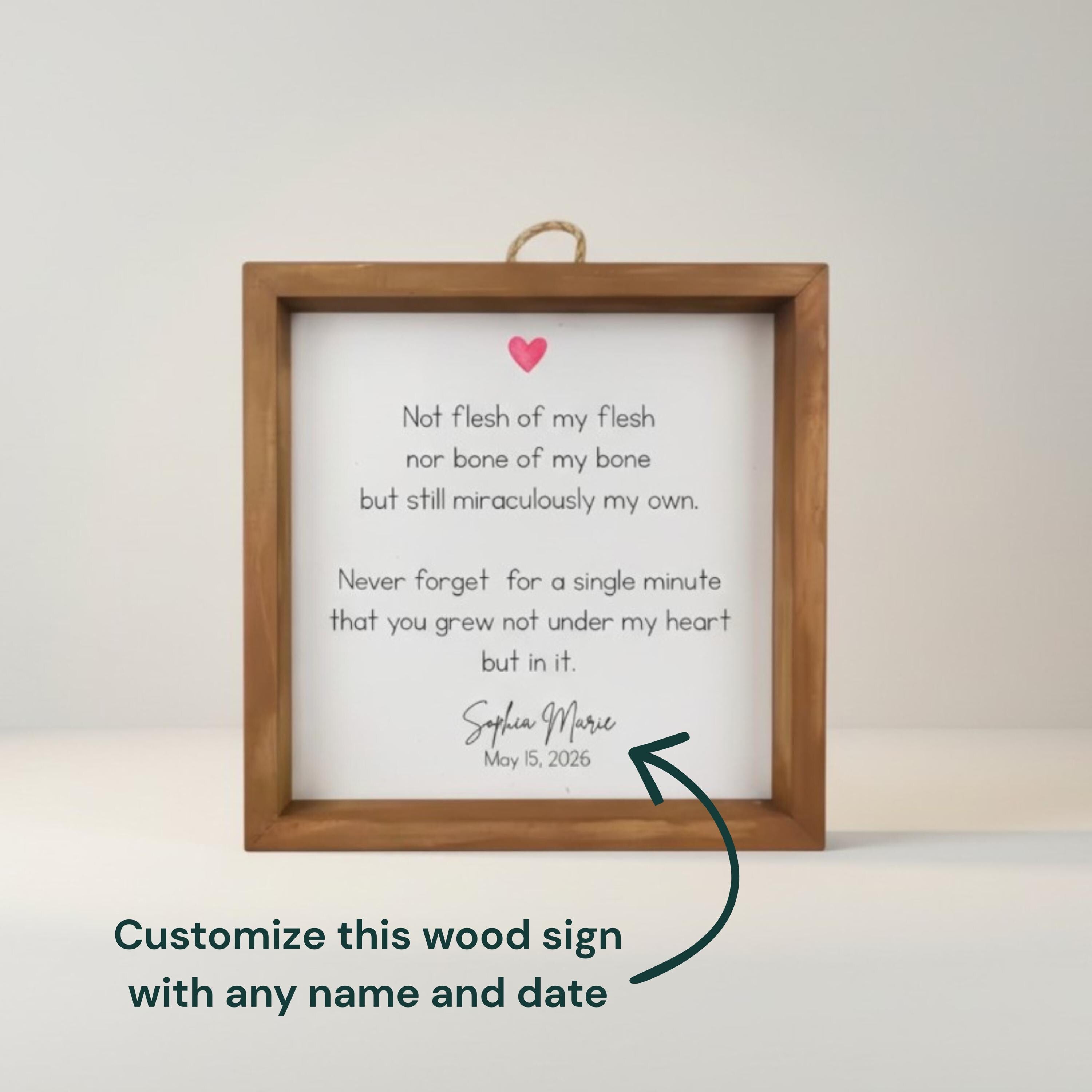 A framed wooden sign with a white background and a printed poem. The poem includes a pink heart graphic and the name "Sophia Marie" with the date "May 15, 2026". The sign is designed to be customized with a name and date.