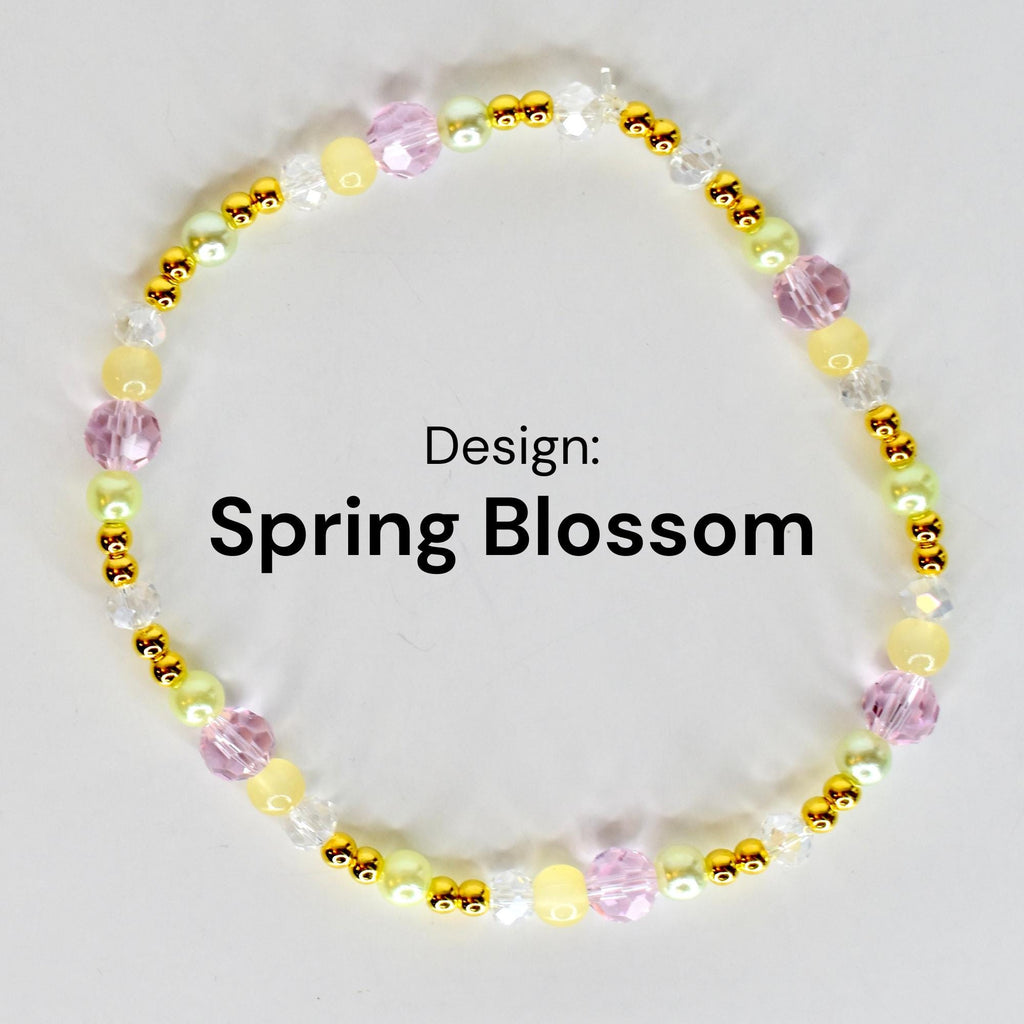 A beaded bracelet with the text "Design: Spring Blossom". The bracelet features a variety of beads in shades of yellow, pink, green, and clear, interspersed with gold-colored accents. The beads are arranged in a circular pattern.