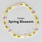 A beaded bracelet with the text "Design: Spring Blossom". The bracelet features a variety of beads in shades of yellow, pink, green, and clear, interspersed with gold-colored accents. The beads are arranged in a circular pattern.