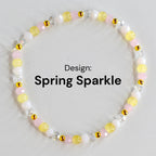 A beaded bracelet with the text "Design: Spring Sparkle." The bracelet features a mix of yellow, pink, white, and clear beads, interspersed with small gold-colored accents. The beads are strung together to form a circular shape.