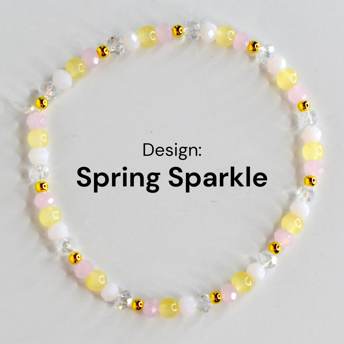A beaded bracelet with the text "Design: Spring Sparkle." The bracelet features a mix of yellow, pink, white, and clear beads, interspersed with small gold-colored accents. The beads are strung together to form a circular shape.
