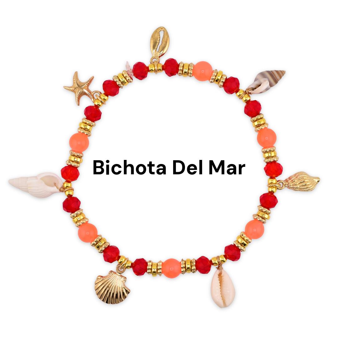 A beaded bracelet with red and orange beads, gold accents, and seashell charms. The bracelet features a starfish, various seashells, and the text "Bichota Del Mar".