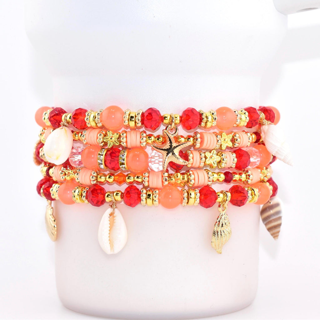 A stack of beaded bracelets in shades of red, coral, and gold. Each bracelet features a mix of beads, including faceted and round styles, with gold accents and seashell charms. A gold starfish charm hangs from one bracelet.