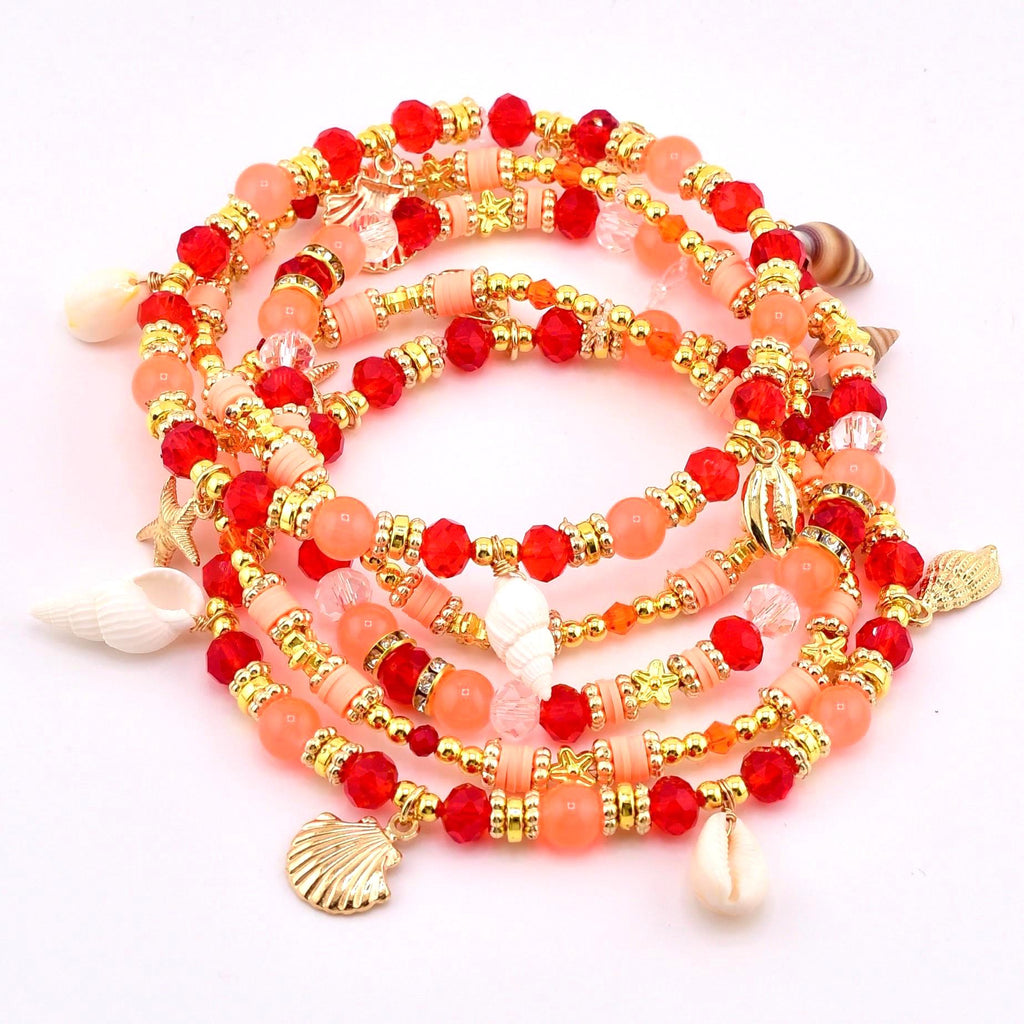 A collection of beaded bracelets in shades of red, peach, and gold. The bracelets are adorned with gold accents, starfish, and seashell charms. The beads are a mix of round and faceted shapes, creating a layered effect.