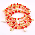 A collection of beaded bracelets in shades of red, peach, and gold. The bracelets are adorned with gold accents, starfish, and seashell charms. The beads are a mix of round and faceted shapes, creating a layered effect.