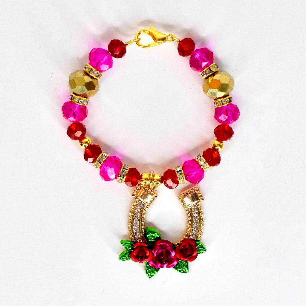 A beaded tumbler handle bracelet with a gold clasp, featuring pink, red, and gold beads. The handle bracelet has a gold horseshoe pendant adorned with rhinestones and a cluster of red roses with green leaves.