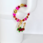 A beaded bracelet with a gold horseshoe charm. The bracelet features pink, red, and gold beads. The horseshoe charm is gold with clear crystals and red roses. The bracelet is displayed on a white surface.