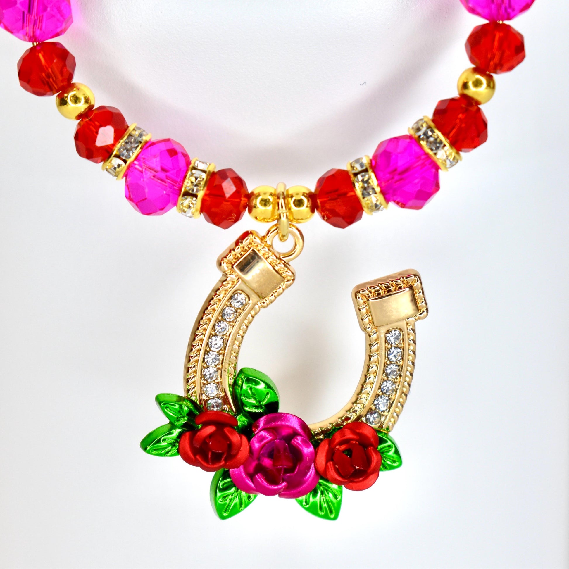 A tumbler handle charm featuring a gold-colored horseshoe pendant adorned with clear crystals and a cluster of red and pink roses with green leaves. The charm has a beaded strand of pink and red beads.